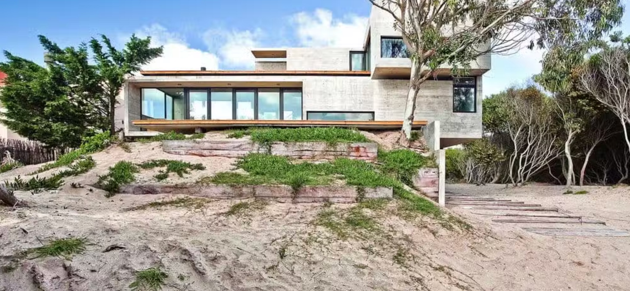 A concrete and timber residence set among coastal dunes and trees